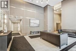 Spacious common area featuring textured wall panels with metallic accents, tile flooring with dark border, tall ceilings, and recessed lighting - 