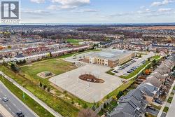 Aerial perspective of a developed neighborhood featuring residential properties, a structured institutional building, an expansive paved lot with court markings, and a large green space with playgroun - 