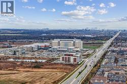 Expansive aerial perspective showcasing a major roadway, numerous commercial and residential structures, a large institutional complex, and distant urban skyline - 