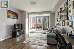 Bright, light-filled living space featuring wood-finish flooring, expansive glass sliding doors opening to a private balcony, and a gallery wall of framed artwork - 