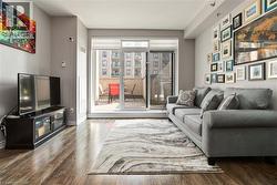 Spacious living area featuring wood-finish flooring, light grey wall tones, and a sliding glass door to a private balcony - 