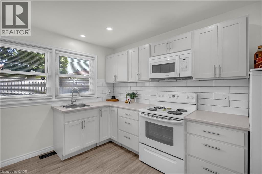 Bright kitchen featuring white shaker cabinetry, light-toned countertops, subway tile backsplash, stainless steel sink with a gooseneck faucet, and wood-finish flooring - 450 Highland Road E, Kitchener, ON