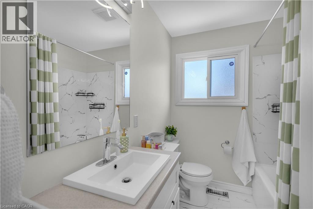 Contemporary bathroom featuring a single vanity with an integrated sink, a white toilet, and a bathtub with a shower - 450 Highland Road E, Kitchener, ON