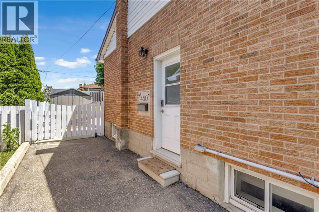 seperate entrance Brick exterior featuring a white entry door, exterior wall lantern, and a white picket fence - 450 Highland Road E, Kitchener, ON