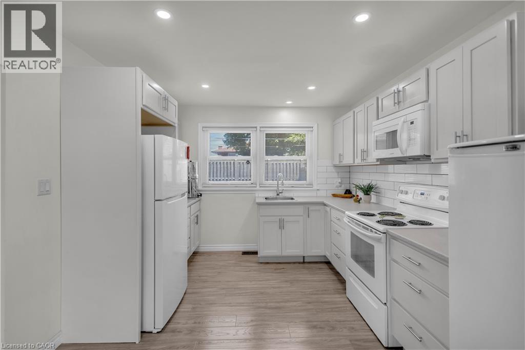 Bright kitchen featuring white cabinetry, subway tile backsplash, light-toned countertops, and wood-finish flooring - 450 Highland Road E, Kitchener, ON