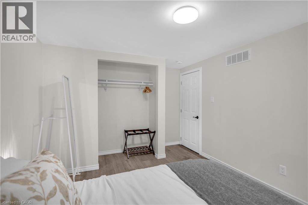 Bedroom featuring wood-finish flooring, recessed closet with hanging rod, white door with black hardware, white baseboards, and a flush-mount ceiling light fixture - 450 Highland Road E, Kitchener, ON