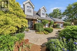Dormer windows, brick and siding exterior, two-car garage, paver walkway, and mature landscaping - 