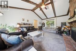Vaulted ceiling with exposed wood beams, brick fireplace with wood mantel, ceiling fan with light fixture, sliding glass door, and wall-mounted shelving - 