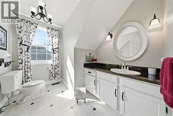 White tile flooring with dark accent squares, a white vanity with panel-front cabinetry, a dark countertop, a circular wall mirror, and a white toilet - 