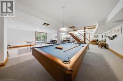 Spacious lower level featuring a pool table, staircase with wood railing, recessed lighting, and a sliding glass door - 
