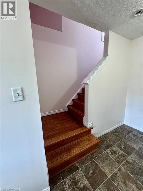 Wood-finish staircase with white trim and railing, complemented by two-tone wall paint and textured ceiling - 452 Beaumont Crescent, Kitchener, ON