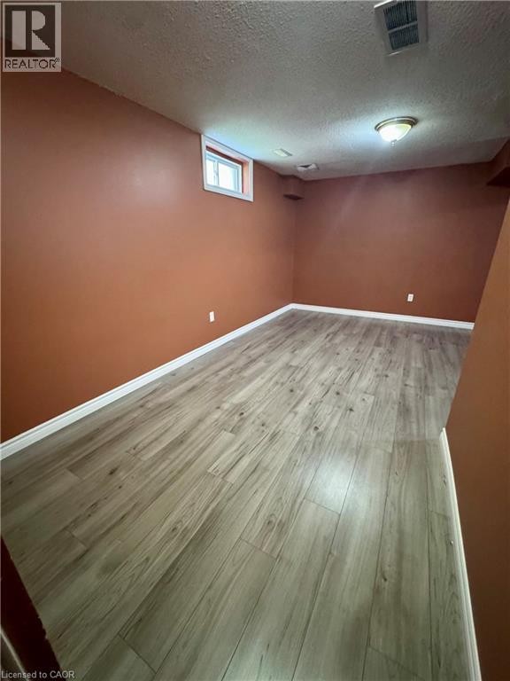 Spacious room featuring wood-finish flooring, warm-toned walls, a single window, and a flush-mount ceiling light fixture - 452 Beaumont Crescent, Kitchener, ON
