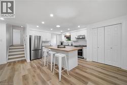 Modern kitchen featuring an island with a wood-finish countertop, stainless steel appliances, white cabinetry, and recessed lighting - 
