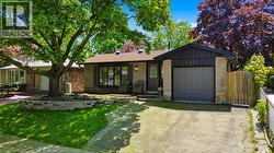 Exterior featuring stone and vertical siding accents, a prominent front picture window, a single-car garage, and a mature front yard tree with a stone-bordered garden bed - 