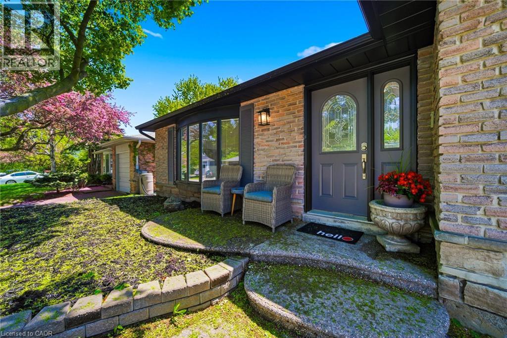 Brick exterior featuring a dark entry door with decorative glass, a bay window, and a concrete entry path with stone retaining walls - 2306 Devon Road, Oakville, ON