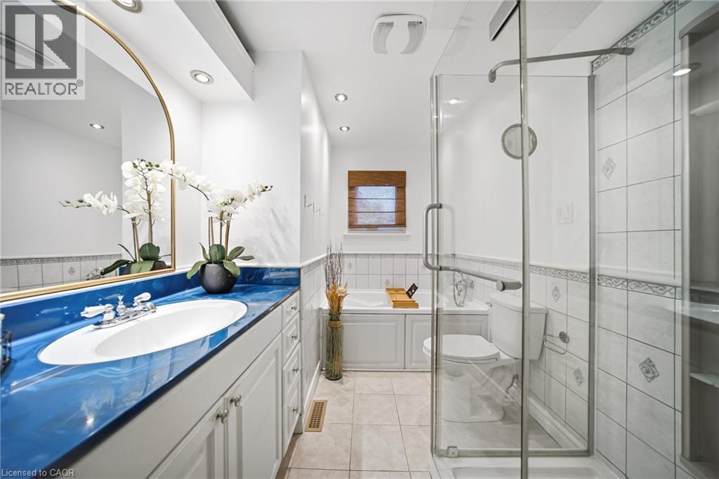 Bathroom featuring a glass-enclosed shower, white tiled walls with decorative accents, and a vanity with a blue countertop - 2306 Devon Road, Oakville, ON