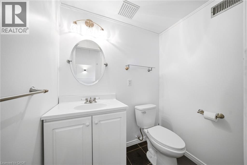 Contemporary bathroom featuring a white vanity with integrated sink, brushed nickel faucet, oval mirror, and dark tile flooring - 2306 Devon Road, Oakville, ON