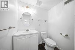 Contemporary bathroom featuring a white vanity with integrated sink, brushed nickel faucet, oval mirror, and dark tile flooring - 