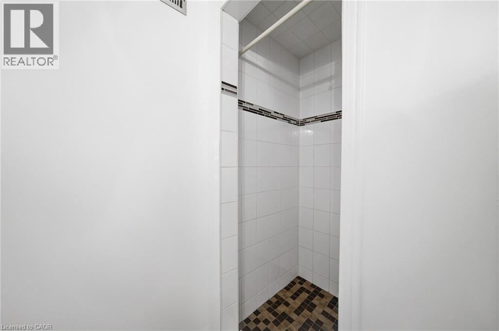 Tiled shower enclosure featuring white square wall tiles, a decorative accent band of horizontal mosaic tiles, and a contrasting mosaic floor in earthy tones - 2306 Devon Road, Oakville, ON
