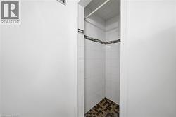 Tiled shower enclosure featuring white square wall tiles, a decorative accent band of horizontal mosaic tiles, and a contrasting mosaic floor in earthy tones - 