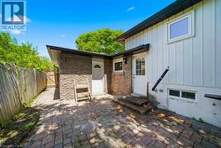 Exterior brick paver patio with a stone facade accent wall, white board and batten siding, and two entry doors - 