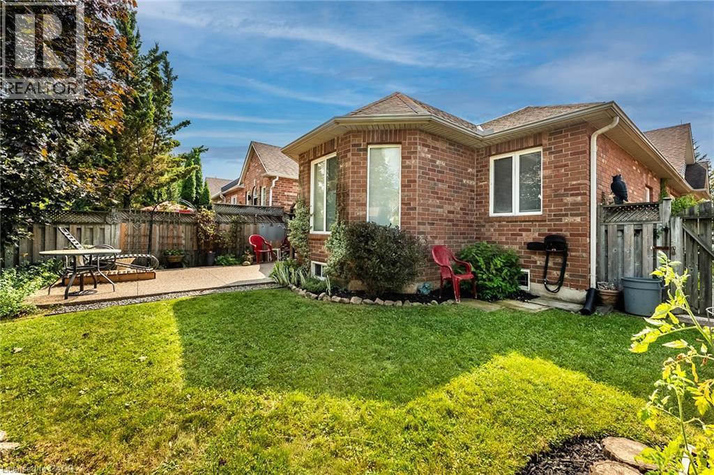 Brick exterior with multiple windows, a manicured lawn, established landscaping, and a fenced backyard with a patio - 159 Thoroughbred Boulevard, Ancaster, ON