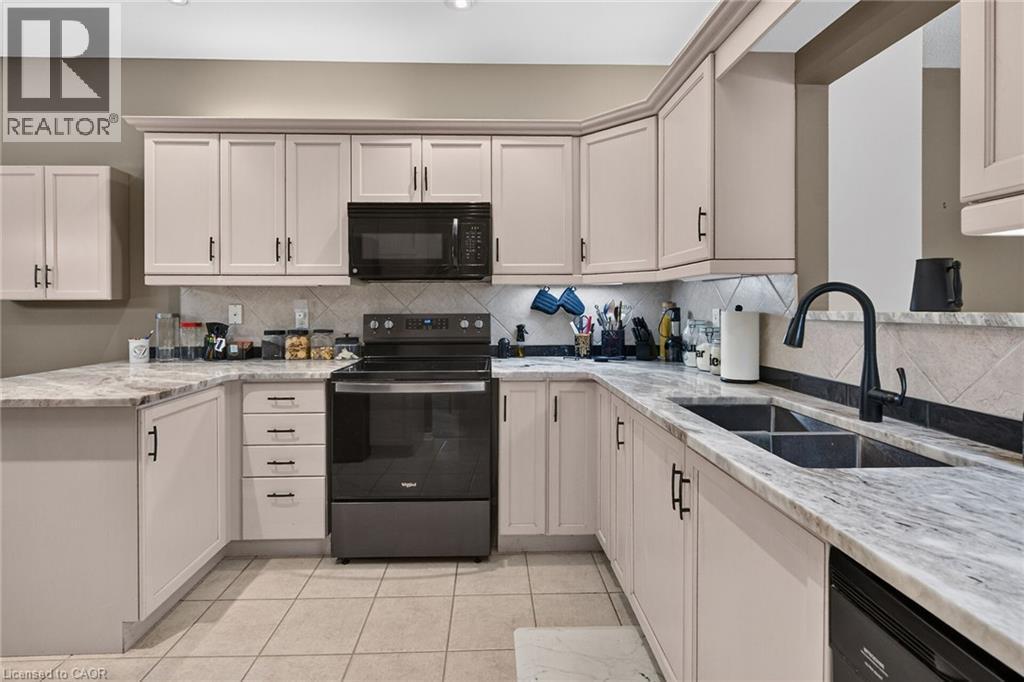 U-shaped kitchen with light-toned cabinetry, light-toned countertops, and a black appliance suite - 159 Thoroughbred Boulevard, Ancaster, ON