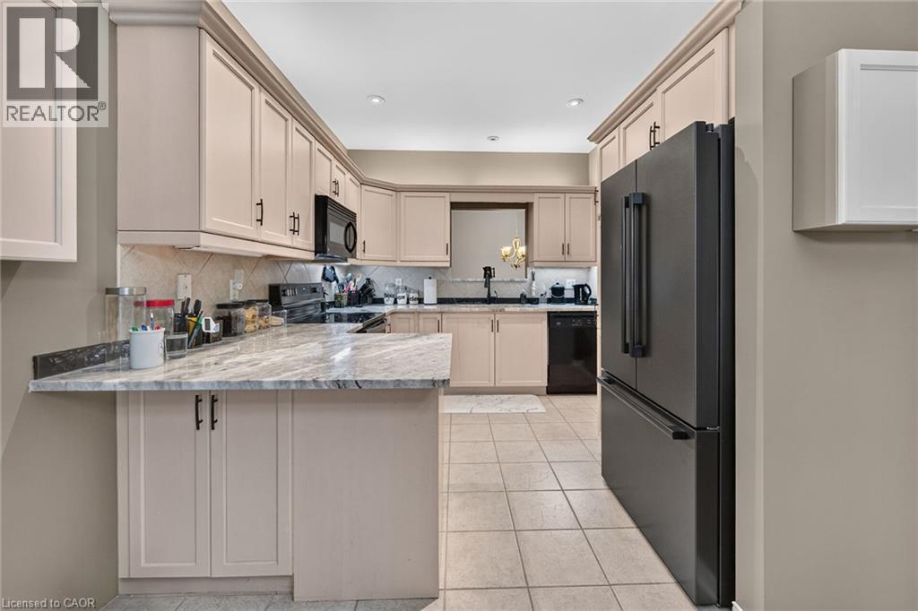 Kitchen featuring light-toned cabinetry with crown molding, matte black appliances, a tile backsplash, and a light-toned countertop with a breakfast bar extension - 159 Thoroughbred Boulevard, Ancaster, ON