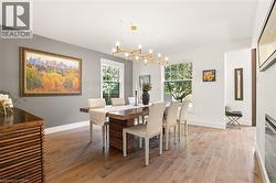 Wood-finish flooring throughout, paired with a contemporary linear chandelier, large windows, and a built-in electric fireplace - 