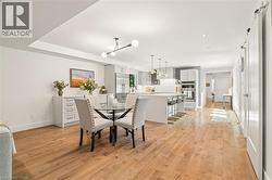 Wood-finish flooring throughout, modern light fixtures, kitchen island with counter seating, stainless steel appliances, and white cabinetry - 