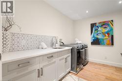 White countertop, geometric tile backsplash, undermount sink with faucet, recessed lighting, and wood-finish flooring - 
