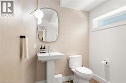 Pedestal sink with chrome faucet, geometric wallpaper, contemporary overhead light fixture, toilet, and an elongated transom window - 