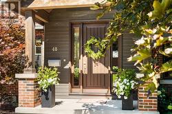 Welcoming entry featuring a dark wood-finish front door with sidelights, flanked by brick pillars and lush landscaping - 