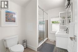 Modern bathroom featuring a walk-in shower with clear glass enclosure, a contemporary vanity with an integrated sink, a rectangular mirror, and wood-finish flooring - 