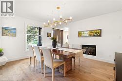 Light wood-finish flooring, built-in linear fireplace, large window with outdoor greenery, and a contemporary chandelier - 