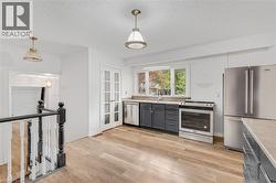 Kitchen featuring wood-finish flooring, dark cabinetry, stainless steel appliances, and a window above the sink - 