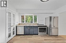 Kitchen featuring wood-finish flooring, stainless steel appliances, ample counter space, dark-toned cabinetry, and a large window - 