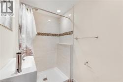 Compact bathroom featuring a walk-in shower with a mosaic tile accent band, a built-in shower shelf, a contemporary wall-mounted sink with a chrome faucet, and recessed lighting - 