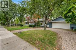 Blue siding exterior with a white garage door, featuring a paver driveway, mature trees, and a concrete sidewalk - 