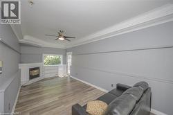 Spacious room featuring wood-finish flooring, a corner fireplace, built-in shelving, and a ceiling fan - 