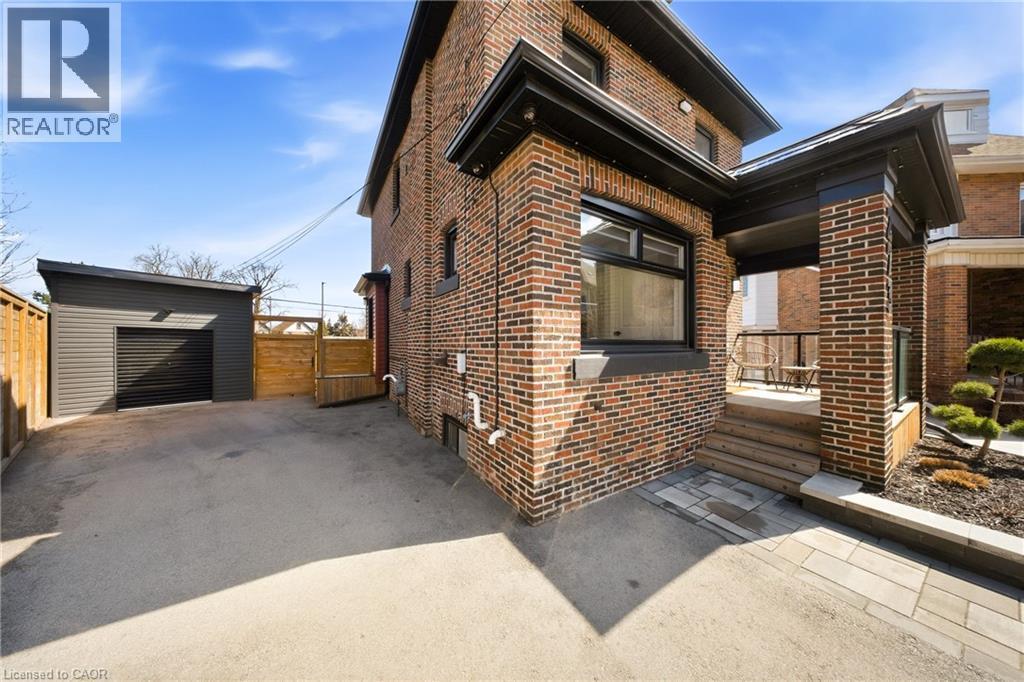 View of side of home with brick siding, an outdoor structure, a patio area, asphalt driveway, and a detached garage - 273 Stinson Crescent, Hamilton, ON