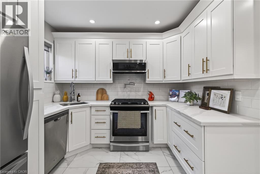 Contemporary kitchen featuring white shaker cabinetry with brushed gold hardware, stainless steel appliances, a white subway tile backsplash, and white stone countertops - 273 Stinson Crescent, Hamilton, ON