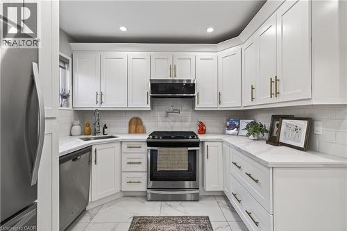 Contemporary kitchen featuring white shaker cabinetry with brushed gold hardware, stainless steel appliances, a white subway tile backsplash, and white stone countertops - 273 Stinson Crescent, Hamilton, ON 