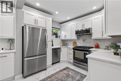 Bright kitchen featuring white shaker cabinetry with gold-toned hardware, stainless steel appliances, a subway tile backsplash, and light-toned countertops - 273 Stinson Crescent, Hamilton, ON 