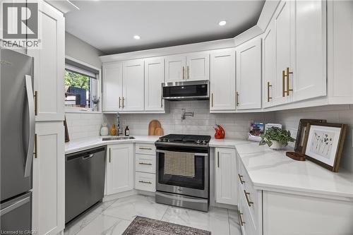 Kitchen featuring white shaker-style cabinetry with gold-toned hardware, stainless steel appliances, white subway tile backsplash, recessed lighting, and white stone countertops - 273 Stinson Crescent, Hamilton, ON 