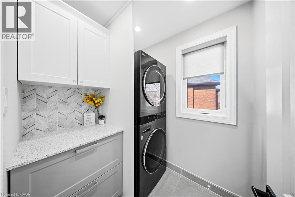 Laundry room with stacked washing machine and dryer, light tile patterned floors, cabinet space, and recessed lighting - 273 Stinson Crescent, Hamilton, ON