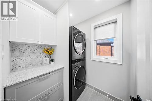 Laundry room with stacked washing machine and dryer, light tile patterned floors, cabinet space, and recessed lighting - 273 Stinson Crescent, Hamilton, ON 