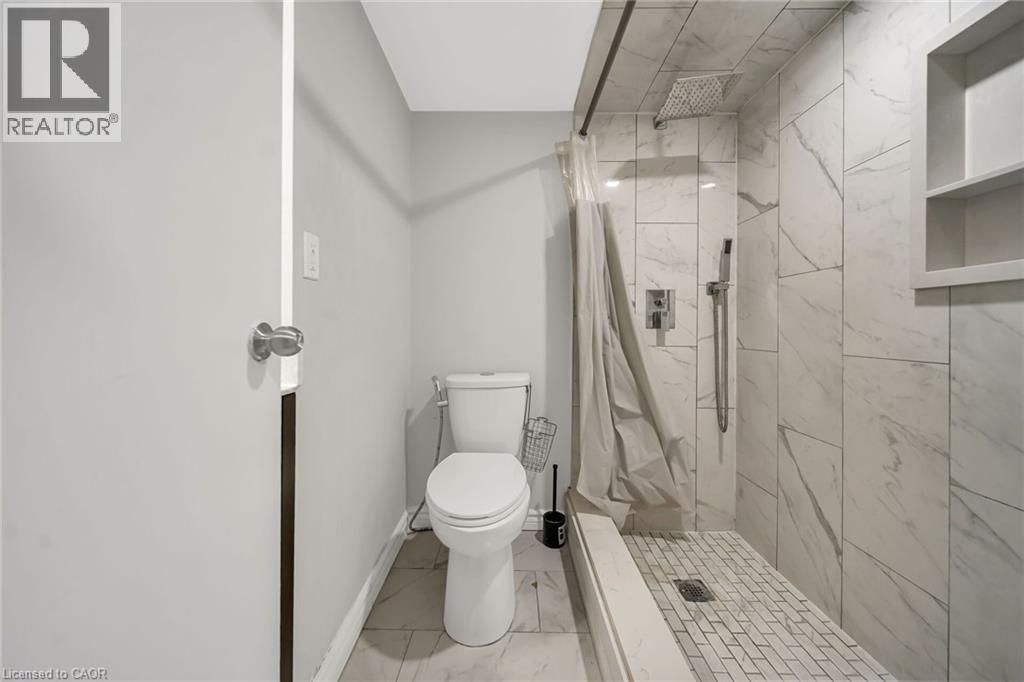Modern primary bathroom featuring a walk-in shower with frameless glass enclosure and linear drain, marble-look tile surround, dual built-in shelving niches, white porcelain toilet, and mosaic tile fl - 284 Cedar Crescent, Cambridge, ON