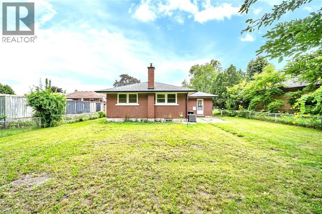 Expansive green space featuring a red brick exterior with white trim windows and a prominent chimney - 284 Cedar Crescent, Cambridge, ON