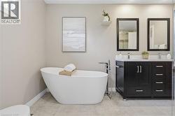 Freestanding soaking tub with floor-mounted faucet, dual vanities with white countertops, and dark wood-finish cabinetry -